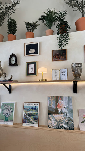 Art wall with framed artwork, plants, and shelves inside Art Café SLC creative studio in Salt Lake City
