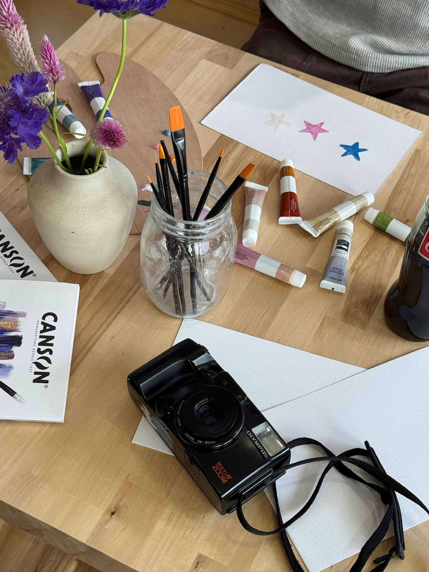 Paint brushes, acrylic paints, and watercolor paper arranged on table at Art Café SLC in Salt Lake City
