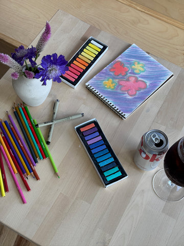 Pastel set, colored pencils, and sketchbook with artwork on table at Art Café SLC in Salt Lake City